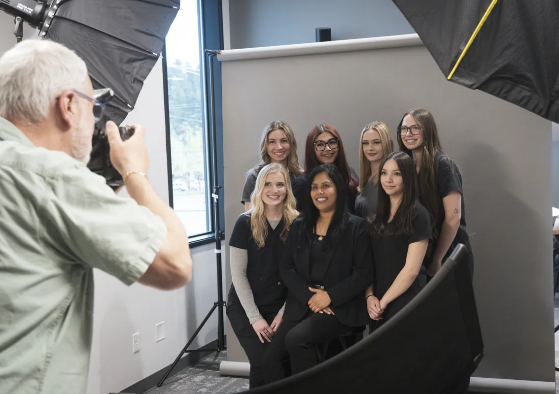 Group photo at McKenzie Dental Center with several dental assistants, studio equipment, and Craig Strobeck taking their photo.