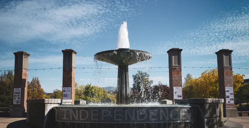 Photo of a waterfall in downtown Independence, OR that has the name written on the bottom and pillars in the back.